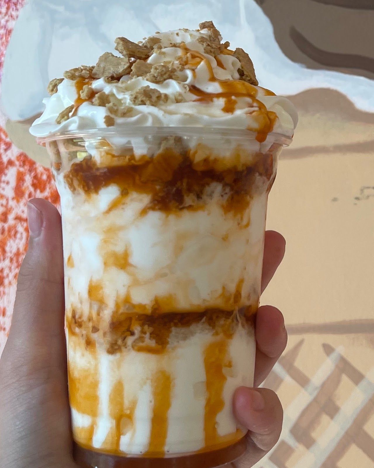 A tall cup of soft serve layered with caramel and cookie crunch, topped with whipped cream
