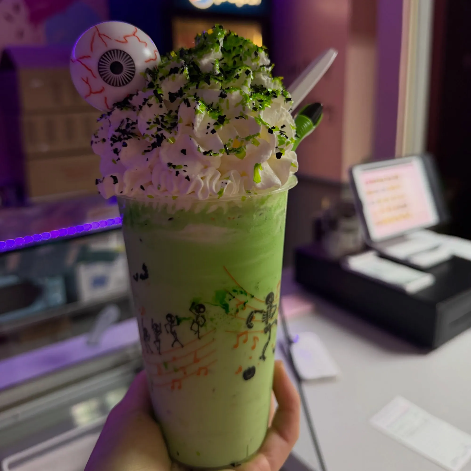 A green shake with an eyeball topper and dancing skeletons on the cup