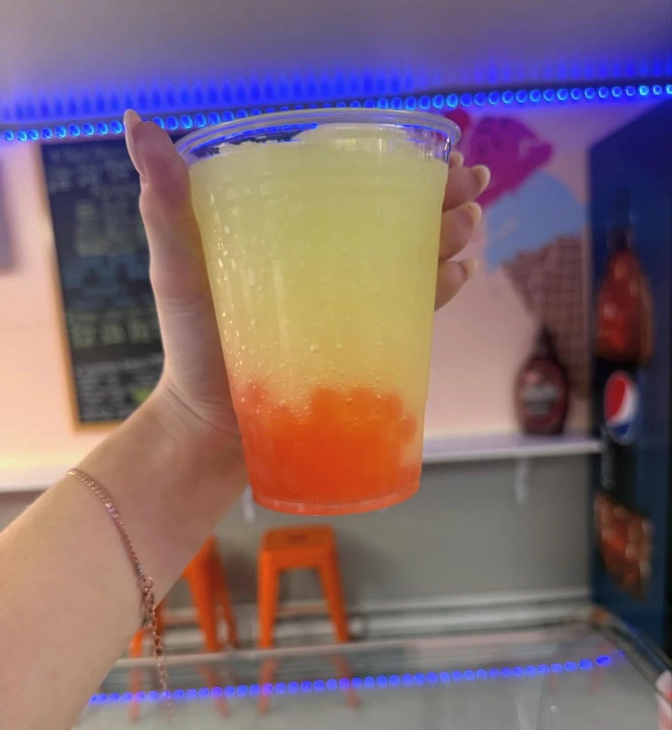 A yellow slushie with orange boba at the bottom, held up in the shop